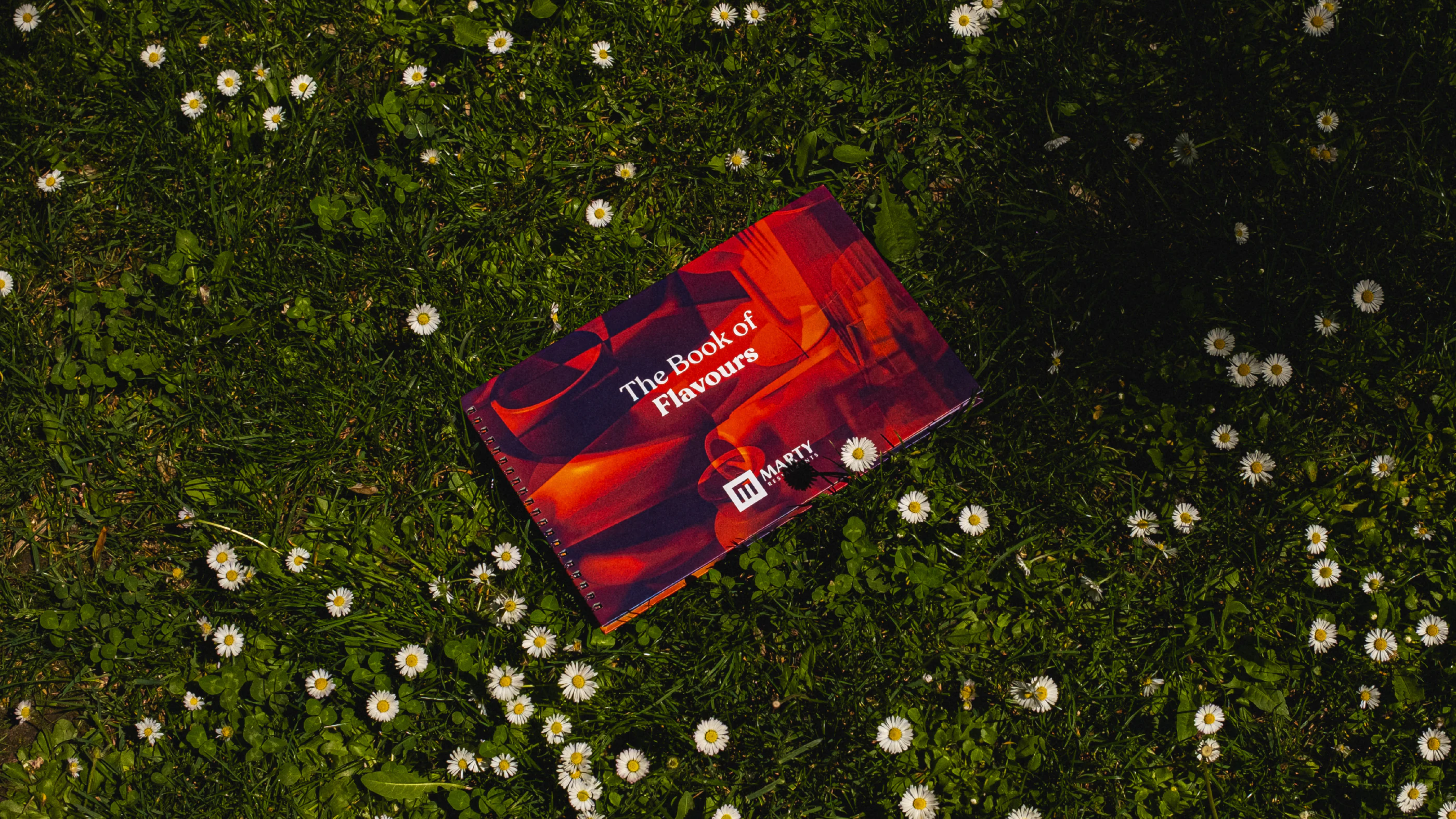 Marty Restaurants menu cover photographed on grass and small white flowers