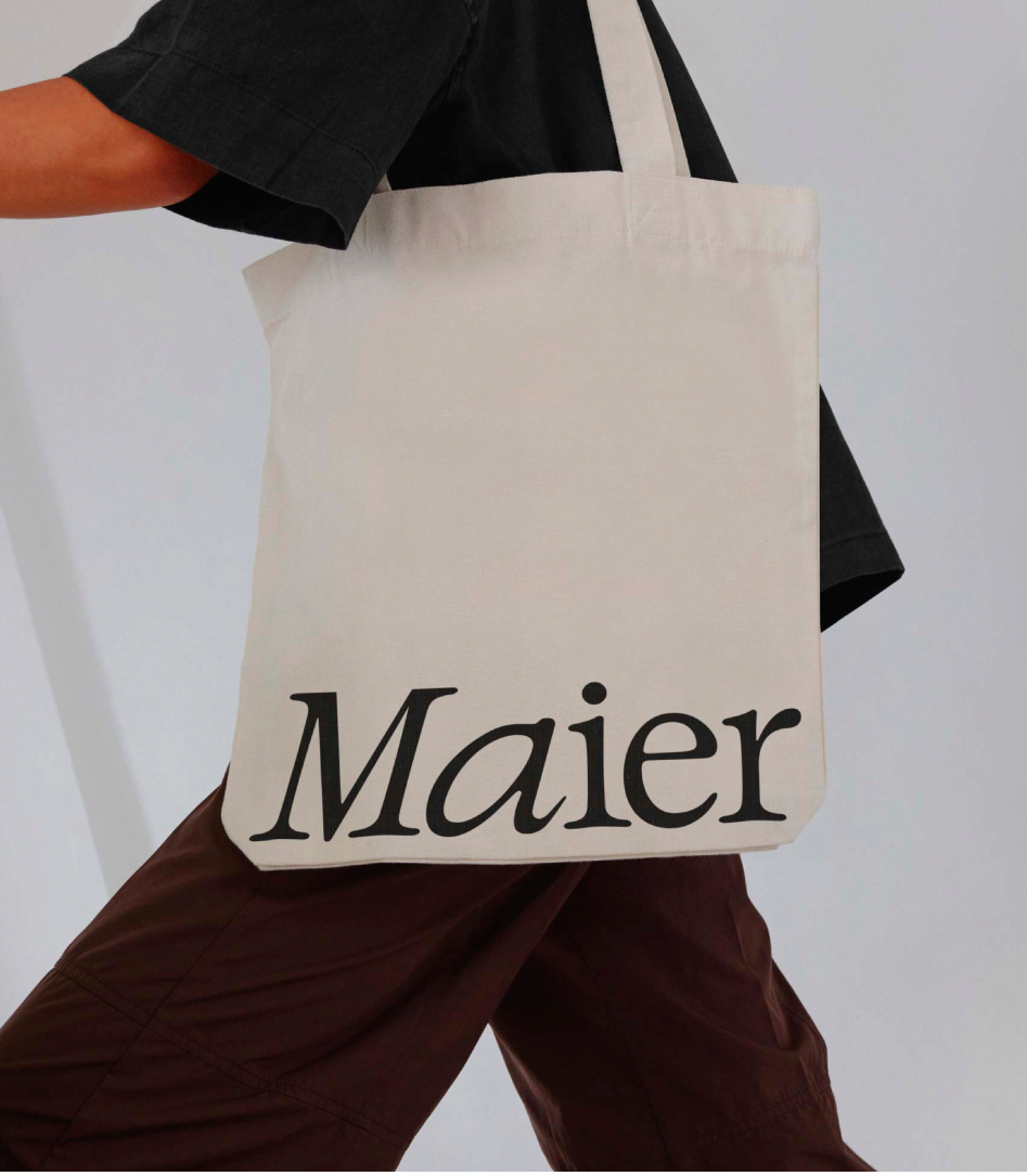 Person carrying a canvas tote bag printed with the Maier wordmark