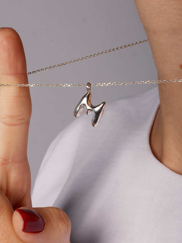 Maier Jewelry M-shaped pendant held against a white shirt